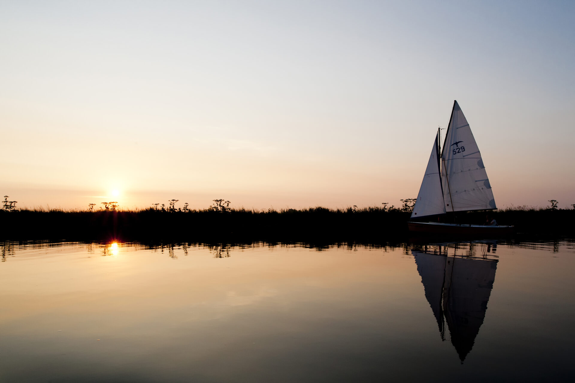 Zeilboot " valk" vaart bij zonsondergang door het van harinxma kanaal richting Grou