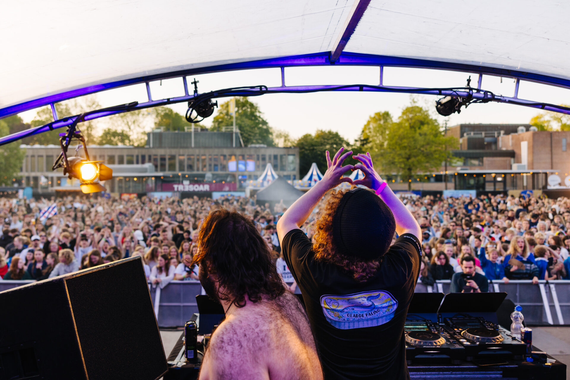 Twee dansende DJ's op een podium met een uitzinnig publiek op de achtergrond