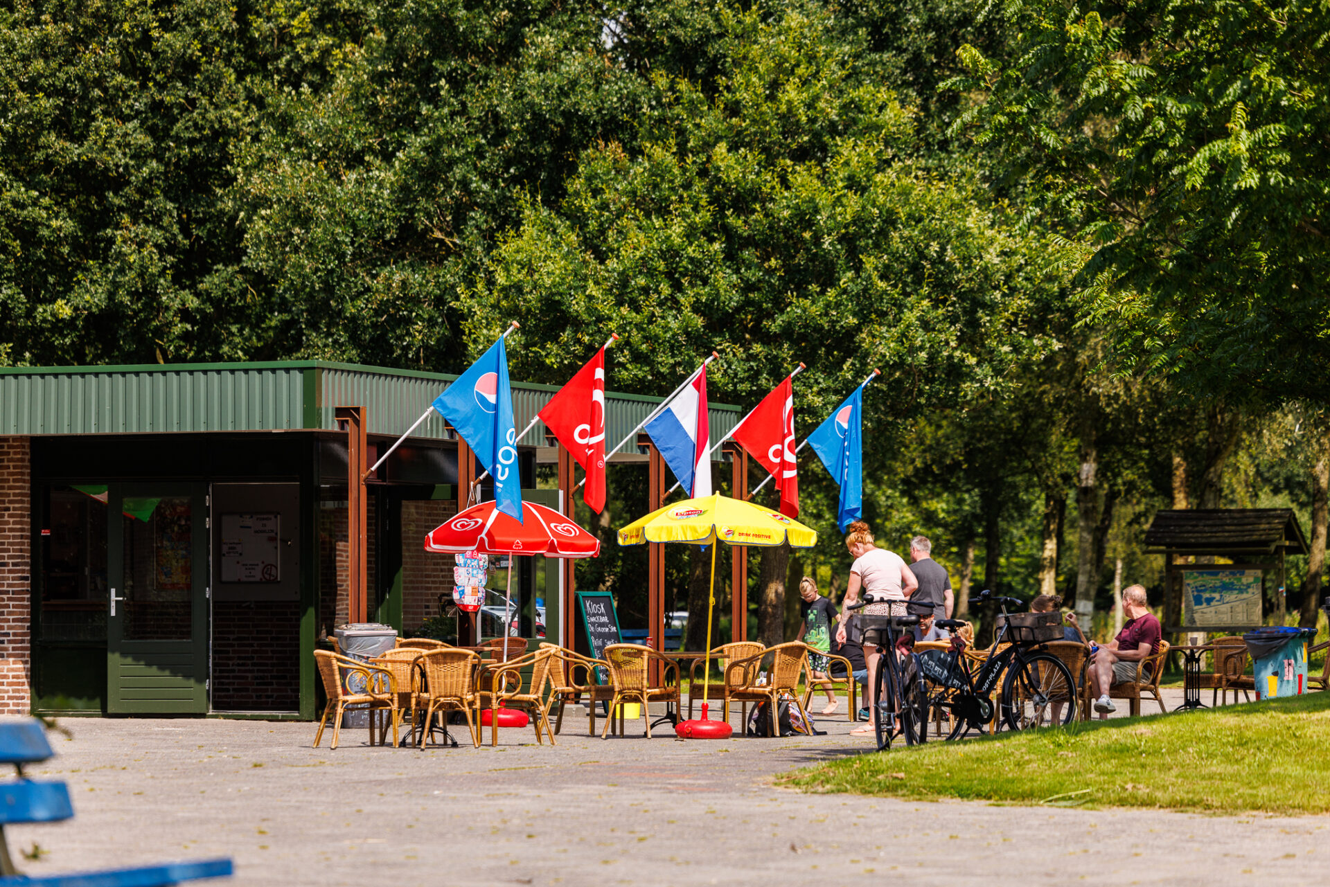 De Groene Ster Campingplek De Kleine Wielen cafetaria om ijsjes en eten te bestellen en een gezin aan het wachten en gekleurde vlaggen