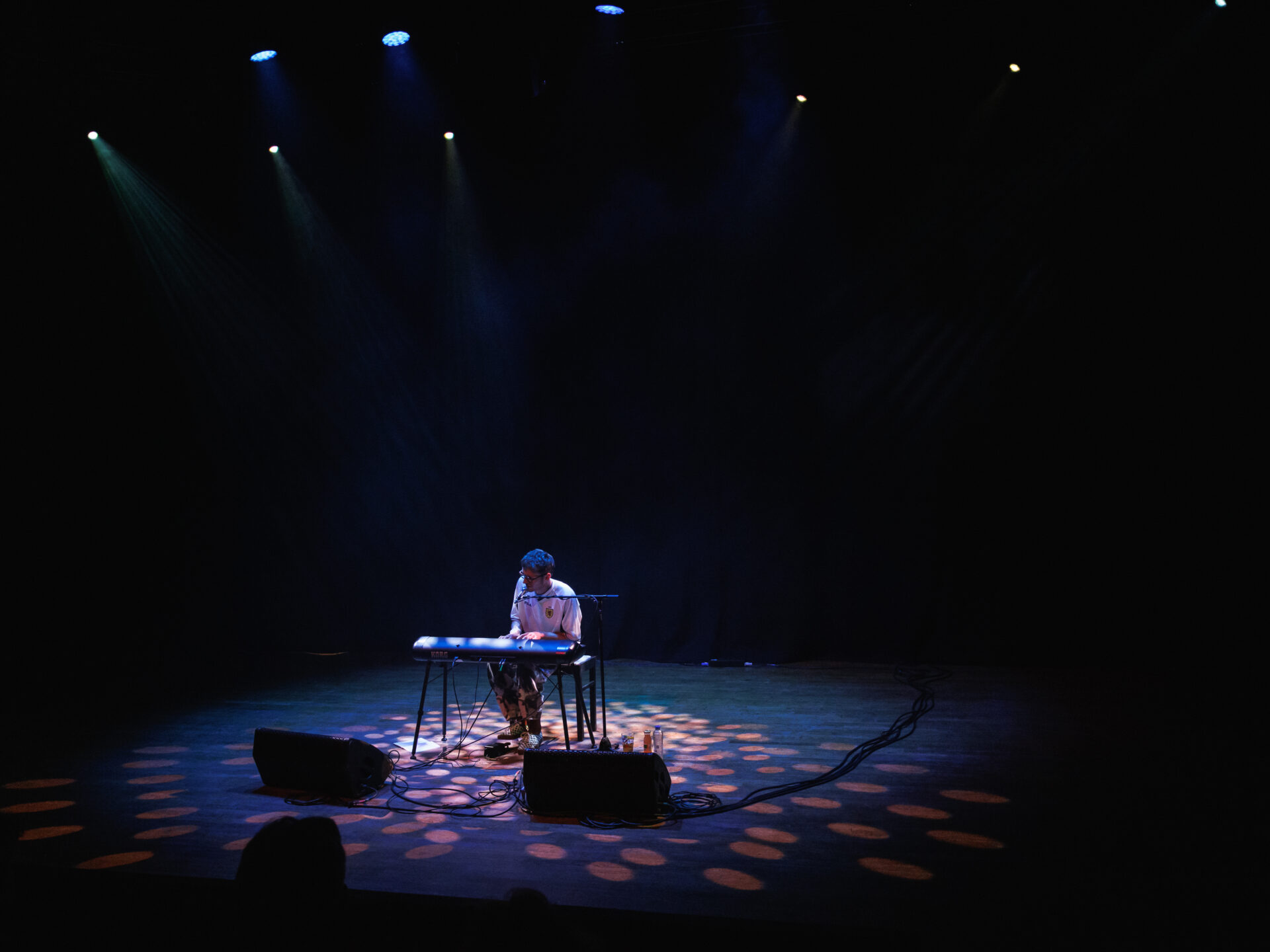 een muzikant bespeelt een elektronisch orgel op een leeg en sfeervol verlicht podium
