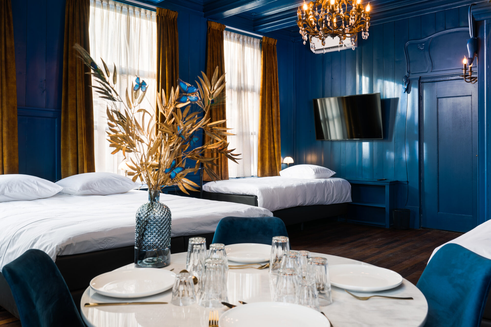 B&B de Olde Signorie grote blauwe hotelkamer met tweepersoons bed en twee eenpersoons bedden en een tafel met bestek en borden om te teen en drinken en zitten