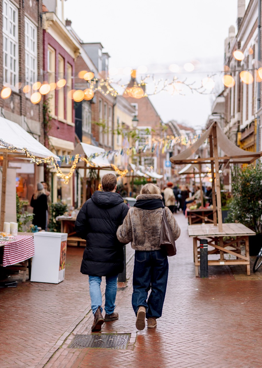 Winkelend koppel op de Boerenmarkt in de Vijzelstraat in december, omringt met kerstverlichting en versiering