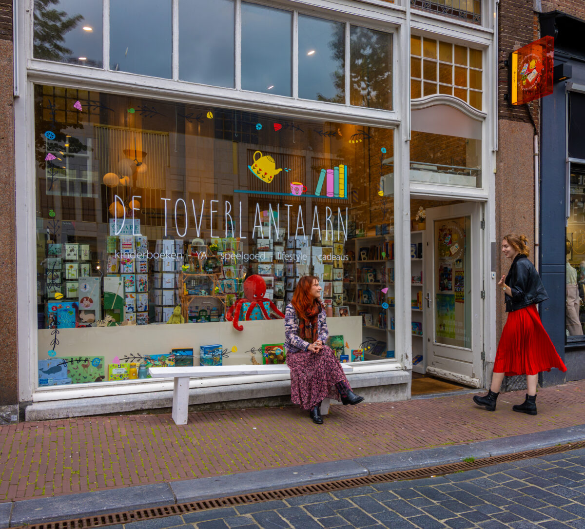 Twee dames zien elkaar voor de etalage van kinderboekenwinkel de Toverlantaarn.