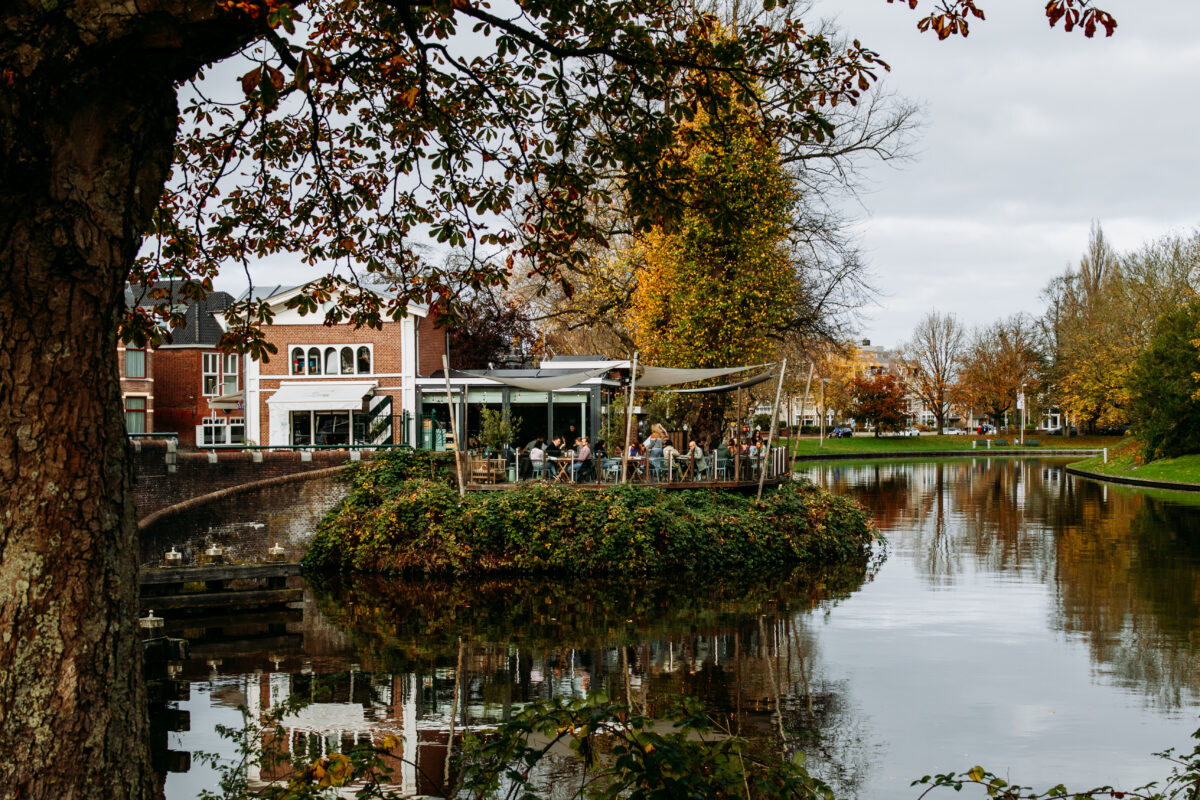 Het herfstige terras van Stek aan de historische stadsgracht. Het terras zit vol en is omringt met herfstblaadjes.