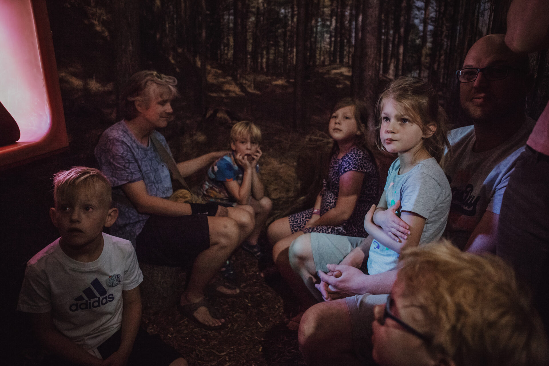 Een groepje jonge kinderen met twee volwassenen luisteren aandachtig naar een verhaal